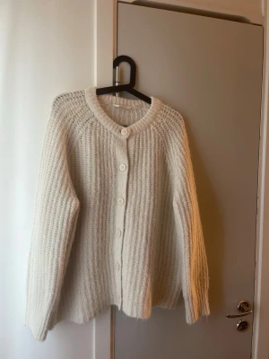 Krämvit stickad kofta med knappar - Mysig krämvit stickad kofta med stora knappar framtill och rund halsringning. Har aldrig kommit till användning 