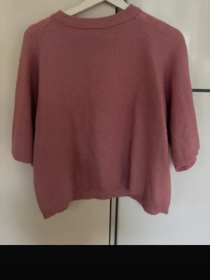 Rosa stickad tröja med trekvartsärm - Mysig stickad tröja i en mjuk rosa nyans. Tröjan har rund halsringning, trekvartsärmar och ribbade kanter vid hals, ärmslut och nederkant. Perfekt för lager på lager och enkel att matcha med jeans eller kjol.