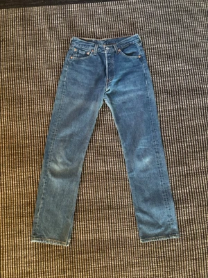 Levis vintage jeans från 1998 - Säljer ett par klassiska blå jeans med rak passform och hög midja. Jeansen har fem fickor, knappgylf och subtila slitningar för en avslappnad look. Perfekta till sneakers eller boots och passar till det mesta i garderoben. Det här är ett par Levis jeans från 1998 från USA och är ett par vintage jeans. Sök mer själva för mer exakta beskrivning med hjälp av bilderna. Det är dock Irregulare märkning i jeansen. Och det är W 29 men dom sitter nog lite med som W 28