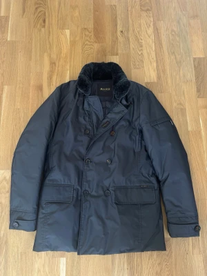 Mörkgrå parkas från MooRER - Mörkgrå skepparkavaj från MooRER med dubbelknäppning och stora bruna knappar. Jackan har en mjuk svart fuskpäls på kragen, slätt vattenavvisande material och två stora fickor framtill. Klassisk och modern look.                              INTESSEKOLL har inte bestämt mig för att sälja jackan så kom med prisförslag!