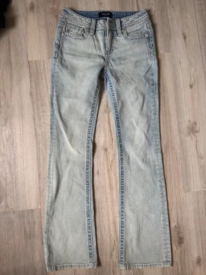 Ljusblå bootcut jeans från Miss Me - Säljer ett par ljusblå bootcut jeans från Miss Me med snygga kontrastsömmar och klassisk femficksmodell. Jeansen har dekorativa detaljer på fickorna och är tillverkade i denim med en lätt tvättad look. Perfekta för dig som gillar en avslappnad men trendig stil. TYVÄRR HAR KNAPPEN DÄR FRAM GÅTT AV I TVÄTTEN! Det går dock super enkelt att fixa och det är därför jeansen säljs billigt! Jeansen i sig är i toppen skick!