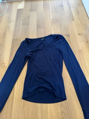 Mörkblå långärmad topp - En enkel och stilren mörkblå långärmad topp med rund halsringning. Tillverkad i ett mjukt och stretchigt material som sitter skönt på kroppen. Perfekt att matcha med jeans eller kjol för en clean look.