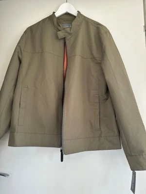 Beige vindjacka från Michael Kors - Den perfekta lättviktsjackan för våren / hösten. Jackan har dragkedja framtill, diskreta sidofickor och en snygg orange meshfoder på insidan. MK-logga i metall bak på ryggen ger en exklusiv.  Storlek: M Mått: enligt MK storleksguiden Bröst: cm: ~ 96,5-101,6  eller (38-40 Inch) Ärmar: cm:~ 83,8-86,4 eller (33-34 Inch).                      Helt ny och oanvänd såklart.     