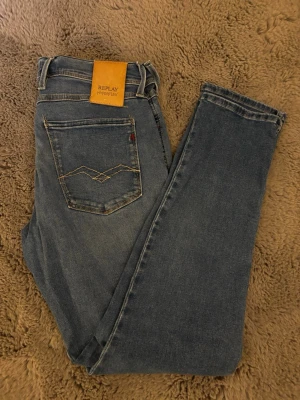 Blå Replay Hyperflex jeans - Snygga blå jeans från Replay Hyperflex med klassisk femficksdesign och dekorativ söm på bakfickan. Jeansen har en skön stretchig passform och ett läderpatch med logga bak i midjan. Perfekta för dig som gillar en avslappnad men trendig stil.