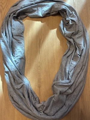 Ljusgrå tubsjal i mjukt tyg 100% bomull  - Säljer en ljusgrå tubsjal i mjukt och stretchigt material. Sjalen är enkel att styla och har en rund, sömlös form som gör den smidig att vira flera varv runt halsen. Perfekt för att addera en chill vibe till din outfit.