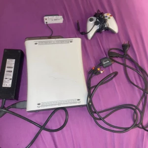 Xbox 360 konsol med spel och tillbehör - Säljer en vit Xbox 360 konsol med tillhörande handkontroll, strömadapter och AV-kablar. Medföljer fem spel: Need for Speed ProStreet, Alan Wake, Saints Row, FIFA 13 och FIFA 14. Spelen kan säljas ensamma.