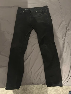 Svarta raka jeans - Säljer ett par svarta jeans med rak passform och klassisk femficksdesign. Jeansen har bälteshällor och knappgylf. Materialet ser ut att vara denim med lite stretch för extra komfort. Perfekta till en avslappnad stil.