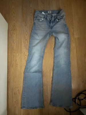 Ljusblå bootcut jeans - Säljer ett par ljusblå bootcut jeans med klassisk femficksdesign och normal midja. Jeansen har utsvängda ben och är tillverkade i denim med en snygg tvättad look. Perfekta för dig som gillar retrostil och vill ha ett par bekväma jeans.