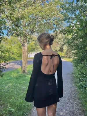 Svart kort klänning med vida ärmar - Snygg svart kort klänning med långa, vida ärmar och figurnära passform. Klänningen har en enkel och stilren design som passar perfekt till många tillfällen. Tillverkad i ett mjukt material som ger en bekväm känsla.