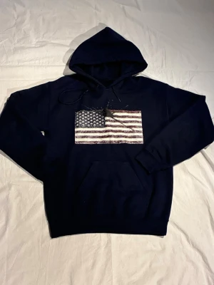 Concrete Inc. USA custom hoodie - Snygg mörkblå hoodie med stor ficka framtill och tryck av den amerikanska flaggan på bröstet. Klassisk huva med dragsko och ribbade muddar vid ärmar och nederkant. Perfekt för en avslappnad och cool stil.