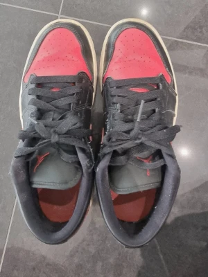 Röda jordans  - Säljer ett par klassiska Nike sneakers i svart och rött läder med vita sulor. Skorna har lågt skaft, svarta skosnören och den ikoniska röda swoosh-loggan på sidan. Perfekta för dig som gillar streetwear och vill sticka ut.