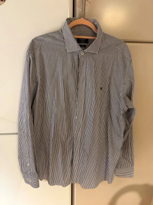 Randig skjorta från Hackett London - Snygg blåvit randig skjorta från Hackett London i slim fit-modell. Skjortan har klassisk krage, långa ärmar och knappar framtill. Perfekt för dig som gillar stilrena och tidlösa plagg.