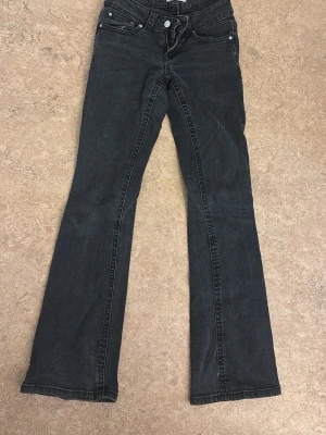grå/svarta jeans - Snygga  grå/svarta bootcut jeans med klassisk femficksdesign och silverfärgade knappar. Jeansen har en lätt utsvängd passform nedtill och kontrastsömmar. Perfekta för dig som gillar en retroinspirerad look.