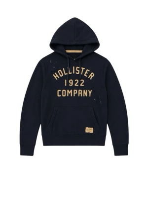 Mörkblå hoodie från Hollister - Mörkblå hoodie från Hollister med gul text 'Hollister 1922 Company' på bröstet. Klassisk känguruficka framtill, justerbar huva med snören och ribbade muddar. Mjuk bomullsblandning och avslappnad passform. Perfekt för en chill och casual stil.