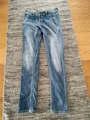 Dondup Blå raka jeans - Säljer ett par klassiska blå dondup jeans med raka ben. Jeansen har fem fickor, bälteshällor och knappgylf. Materialet är denim i bomull och passformen är avslappnad men ändå smal. Perfekta till vardagslooken! Storlek 29
