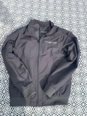 Grå vindjacka från Sail Racing - Snygg grå vindjacka från Sail Racing med GORE-TEX-material. Jackan har dragkedja framtill, ribbade muddar och diskret logga på bröstet. Perfekt för blåsiga dagar och enkel att matcha med olika outfits. Använd ett par gånger men passar inte längre var inte rädd att fråg 