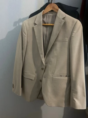 Beige kostym med kavaj och byxor storlek S på kavaj 44 på byxa - Snygg beige kostym HELA FÖR 600kr NY PRIS 200kr med klassisk kavaj och matchande byxor. Passar utmärkt till sommaren, student bal och vardagliga sammanhang! Passar Kavajen har två knappar, fickor med lock och bröstficka. Perfekt för dig som vill ha en stilren och tidlös look. Materialet känns mjukt och lätt, vilket gör den bekväm att bära. Storlek s på kavajen och 44 på byxorna! Prisa kan diskuteras bara att höra av dig vid en fråga!!
