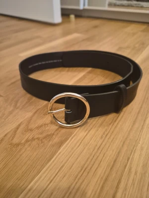 Svart bälte med rund silverspänne - Stilrent svart bälte med ett runt guldspänne från H&M. Bältet har en klassisk design och passar perfekt till jeans eller byxor. Enkelt att matcha med olika outfits. PRIS KAN DISKUTERAS! Kom gärna med prisförslag och frågor!😊🌸