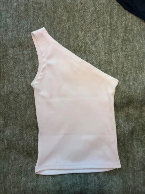 Vit oneshoulder topp - Säljer en oneshoudler topp. Väldigt fin men har en liten fläck i mitten som man ser knappt, annars i bra skick ☺️