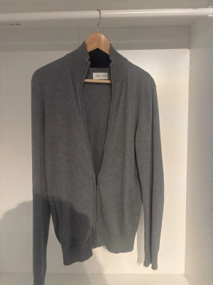 Pier one zip tröja - En stilren grå ziptröja med hög ribbad krage och långa ärmar. Tröjan har dragkedja framtill och ribbade muddar vid ärmslut och nederkant. Perfekt att slänga på sig över en t-shirt för en clean look.