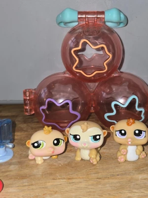 Littlest Pet Shop, Petriplets hamster set  - Tre söta Littlest Pet Shop figurer i beige och bruna toner med stora ögon och detaljer i gult och orange. Medföljer en rosa plastväska med blått handtag och färgglada stjärnformade öppningar, perfekt för förvaring eller lek.