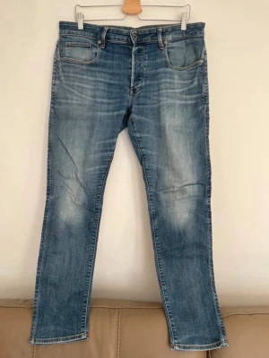G-star raw jeans  - Snygga blå slim fit jeans med slitna detaljer och ljusa partier på låren. Klassisk femficksmodell med knappgylf och kontrastsömmar. Perfekta för en avslappnad och trendig look. Tillverkade i denim med skön stretch.
