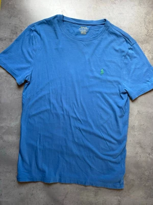 Blå t-shirt från Polo Ralph Lauren - Snygg blå t-shirt från Polo Ralph Lauren med klassisk grön logga broderad på bröstet. Modellen har rund halsringning och korta ärmar. Tillverkad i mjuk bomull och har en slim fit passform som sitter snyggt.