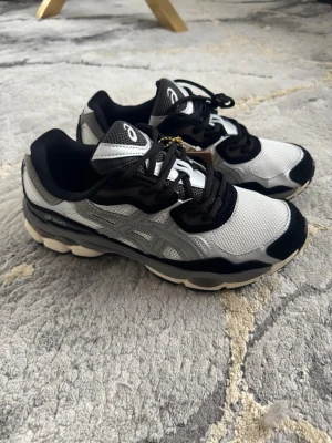 Svarta och vita Asics sneakers - Snygga sneakers från Asics i svart och vitt med mesh- och syntetmaterial. Skorna har en chunky sula, svarta detaljer och vita partier på ovandelen samt Asics-logga på sidan och tungan. Perfekta för dig som gillar sportig och trendig stil.