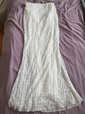 Vit lång spetskjol med foder - Säljer en elegant lång kjol i vit spets med mjukt vitt foder under. Kjolen har en rak passform som faller snyggt och är perfekt för dig som gillar romantisk och stilren look. Spetsmaterialet ger en extra lyxig känsla och kjolen är lätt att matcha.