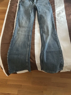 Blå bootcut jeans med breda ben - Säljer ett par klassiska blå bootcut jeans med breda ben och femficksmodell. Jeansen har en snygg tvättad look och är tillverkade i denim. Perfekta för dig som gillar en avslappnad och trendig stil.