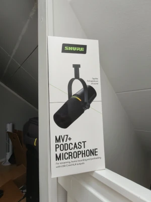 Shure MV7+ Podcast Mikrofon - Shure MV7+ podcast mikrofon i svart, perfekt för streaming, hemmainspelning och podcasting. Mikrofonen har både USB-C och XLR-utgångar för flexibel användning. Modern design med robust metallkropp och tydlig logga på sidan.