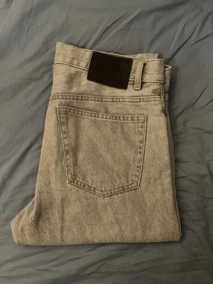 Ljusgrå raka jeans - Säljer ett par ljusgrå jeans med rak passform och klassisk femficksdesign. Jeansen har en svart patch bak i midjan och är tillverkade i ett slitstarkt denimtyg. Perfekta för dig som gillar en clean och enkel stil. Bara skriva om man vill ha mått!
