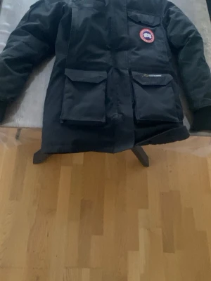 Svart dunjacka från Canada Goose - Säljer en svart dunjacka från Canada Goose med klassisk patch på bröstet. Jackan har stora fickor framtill, quiltad insida och muddar vid ärmsluten. Perfekt för kalla vinterdagar och riktigt varm tack vare dunfyllningen. Sitter fint 