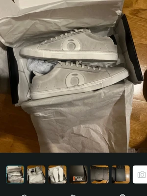 Vitgråa sneakers från Oliver Cabell - Stilrena vita sneakers från Oliver Cabell med lågt skaft och svart detalj på hälen. Skorna har en rundad tå, vita snören och en diskret logga på sidan. Tillverkade i slätt läder för en clean look. Kostar 2000 kr original pris 