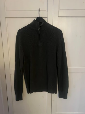 Mörkgrå stickad halvzip från Dobber - Mörkgrå stickad tröja från Dobber med halv dragkedja och hög krage. Ribbstickad struktur och långärmad modell som ger en clean och stilren look. Perfekt till lager på lager under kyliga dagar.