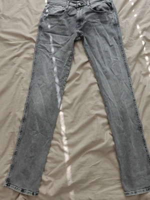 Replay jeans - Säljer ett par grå jeans med rak passform och klassisk femficksdesign. Jeansen har normal midja och subtila slitningar för en avslappnad look. Perfekta för dig som gillar en stilren och enkel vibe.