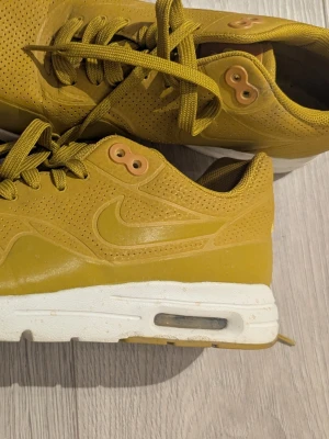 Gula Nike Air Max sneakers - Snygga gula Nike Air Max sneakers med vit sula och synlig luftbubbla. Ovandelen är i perforerat material för extra ventilation och har klassisk Nike-logga på sidan. Skorna har matchande gula skosnören och detaljer i gult och beige.