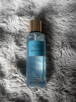 Victoria's Secret Aqua Kiss mist - Fräsch body mist från Victoria's Secret i doften Aqua Kiss. Flaskan är genomskinlig med blått innehåll och har ett stilrent blått etikett och ett guldigt lock. Rymmer 250 ml och är perfekt att spraya på kroppen för en uppfriskande känsla.
