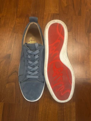 Louboutin Sneakers - Snygga blå sneakers i mocka från Christian Louboutin med klassisk röd sula och diskret logga på insidan. Skorna har rund tå, matchande blå skosnören och vit yttersula. Perfekta för dig som vill ha en stilren och exklusiv look.