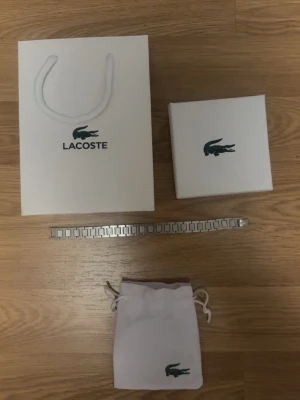 Silverfärgat armband från Lacoste - Stilrent armband i silverfärgad metall från Lacoste. Länkarna har en modern, fyrkantig design och armbandet levereras med originalpåse och ask med Lacoste-logga. Perfekt accessoar för dig som gillar minimalistisk och sportig stil.