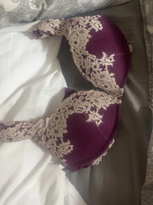 Lila intimissimi bh med spetsdetaljer - Snygg lila bh med vadderade kupor och dekorativa spetsdetaljer i vit över kuporna och axelbanden. Bh:n har en feminin design och ger bra stöd. Materialet är en mix av spets och slät textil för en bekväm känsla.