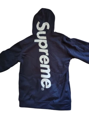 Mörkblå Supreme hoodie med stor logga - Säljer en niche mörkblå hoodie från Supreme med stor vit logga längs ryggen som passar perfekt till de sköna sommarkvällarna. Jag har aldrig använt den, priset är ej hugget I sten så tveka ej på buda🙌
