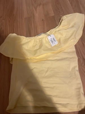 Gul offshoulder topp med volang - Söt ljusgul offshoulder topp med bred volang runt axlarna. ej använd, prislapp kvar. storlek 146/152 men passar som en XS