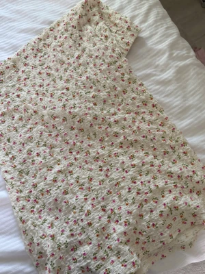 Vit blommig långkjol - Söt vit långkjol  med små rosa och gröna blommor. Klänningen har en lätt strukturerad yta och ett romantiskt, somrigt mönster. 