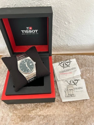 Tissot PRX Powermatic 80 40mm Grön Urtavla - Snygg Tissot PRX klocka med grön urtavla och datumvisnin (40mm). Klockan har ett stilrent armband i silverfärgat stål och kommer i originalbox. Perfekt accessoar för dig som gillar klassisk och modern design. Inga tecken av slitage på dial,bezel,caseback däremot är armbandet lite slitet men svårt att se förutom i närbild och tydligt ljus som visat på bilder. Ingår låda,extralänk samt kvitto.