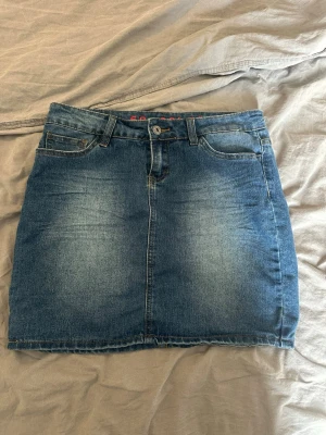  blå jeanskjol - Säljer en klassisk blå jeanskjol. Kjolen har en snygg tvättad look och rå kant nertill för en trendig vibe. Perfekt att matcha med sneakers eller boots för en cool och avslappnad stil