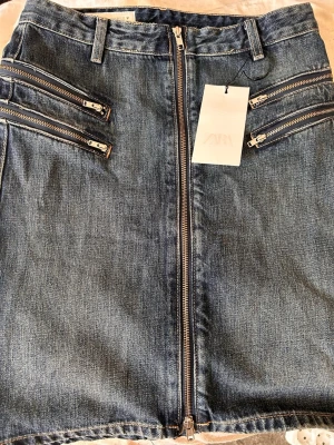 Jeanskjol med dragkedjor - Pris kan diskuteras!!  Säljer en blå jeanskjol med flera coola dragkedjor framtill och bälteshällor i midjan. Kjolen har en rak passform och är i klassisk denim med snygga detaljer. Perfekt för dig som gillar en edgy och trendig stil.