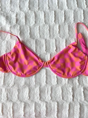 Rutig bikiniöverdel i rosa och orange - Snygg bikiniöverdel med rutigt mönster i rosa och orange. Modellen har bygel och tunna axelband. Perfekt för strandhäng eller poolparty. Materialet känns som syntet, vilket torkar snabbt och är bekvämt att bära.