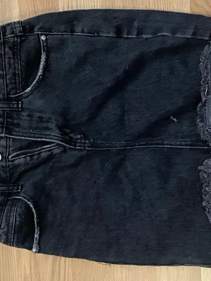 Svart jeanskjol med rå kant - Säljer en svart jeanskjol med rå, fransig kant nertill och klassiska fickor fram. Kjolen har dragkedja och knapp framtill och är i en kort modell. Perfekt till sneakers eller boots för en cool vardagslook. En liten fläck som kan tas bort på framsidan 