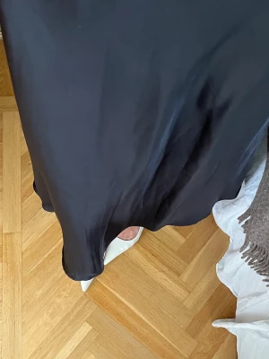 Svart långkjol i satin - Säljer en svart/mörkblå långkjol i glansigt satinmaterial. Kjolen har en enkel och stilren design med lätt utsvängd form som ger ett snyggt fall. 